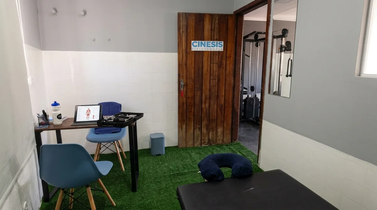 Ambiente da sala de atendimento da Cinesis, com piso em grama sintética e maca de fisioterapia.