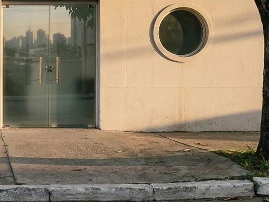 Entrada de vidro de um prédio clínico, com parede clara e uma janela redonda ao lado da porta